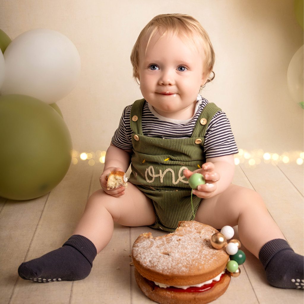 Baby celebrating a first birthday cake smash with balloons and a naked fruit cake